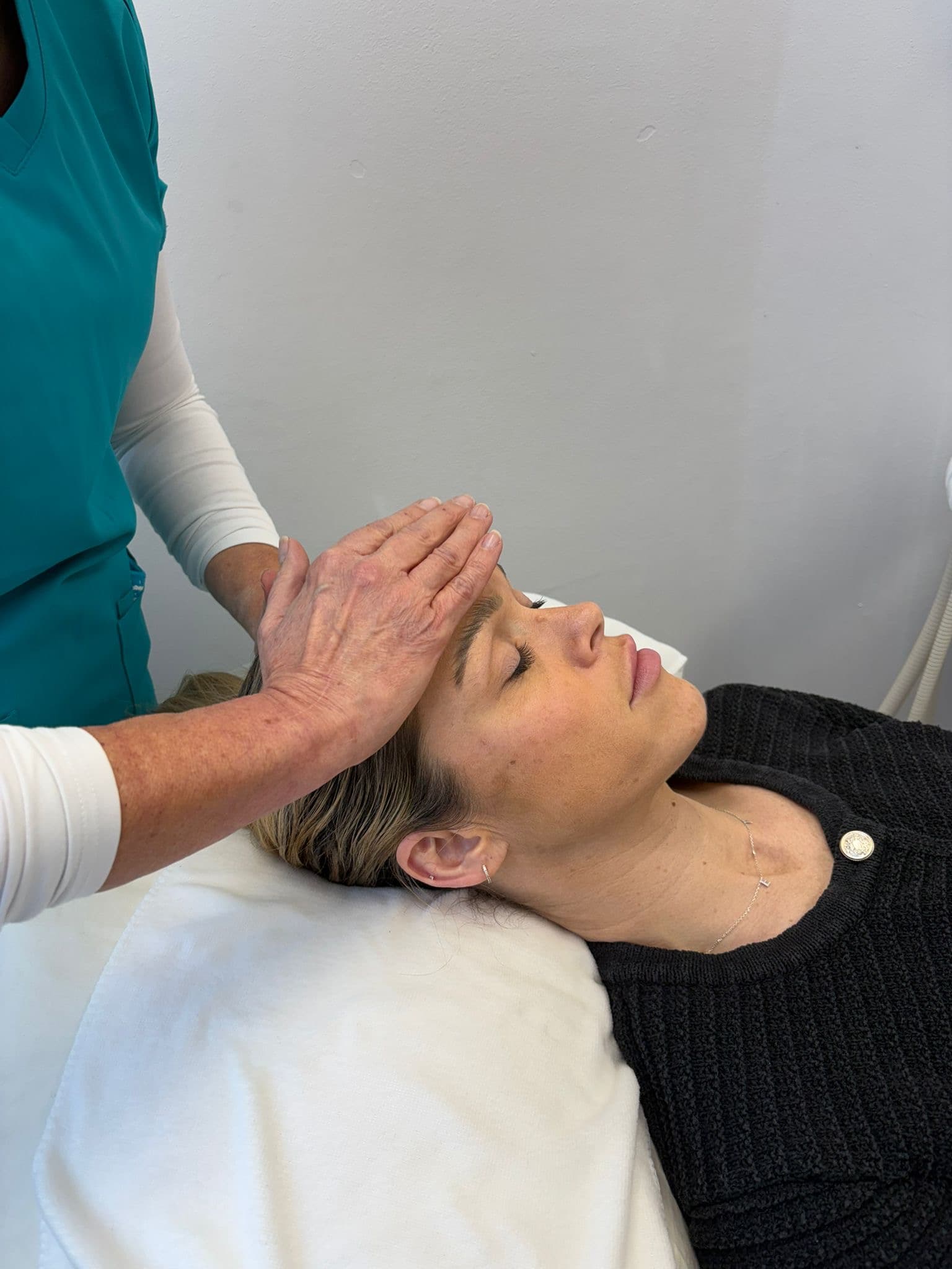 Practitioner's hands rest on the forehead of a woman lying with her eyes closed.