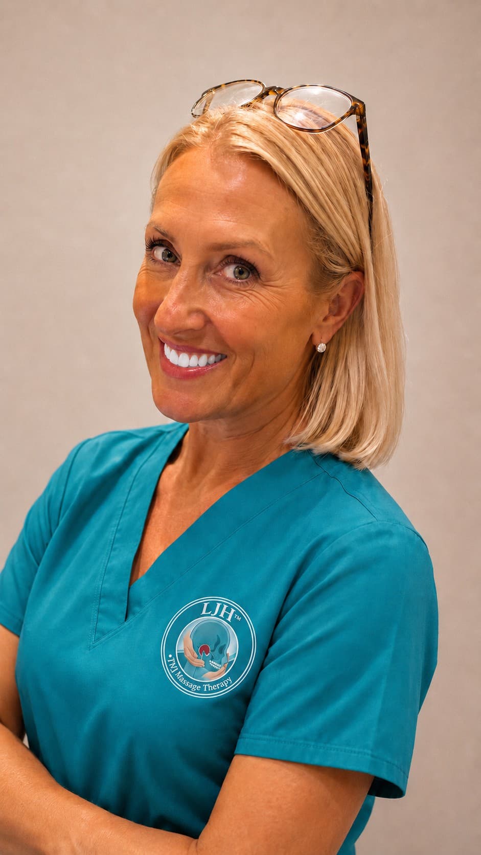 Smiling blonde woman in teal scrubs with a TMJ Massage Therapy logo.