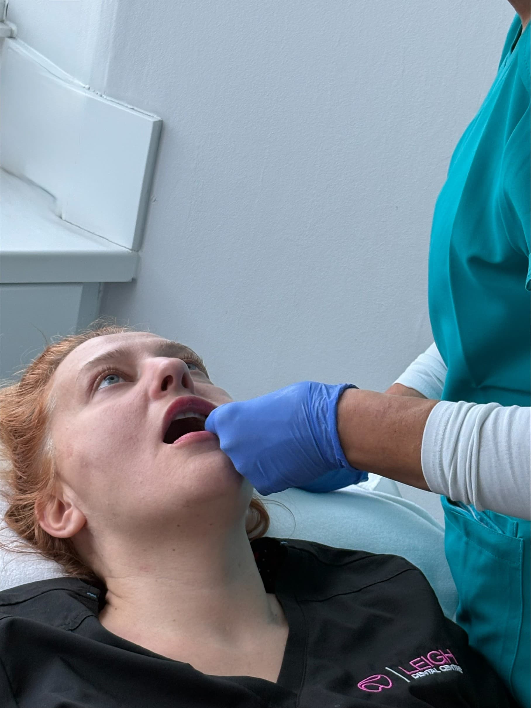 Professional in blue gloves examining a woman's mouth during a dental or facial treatment.