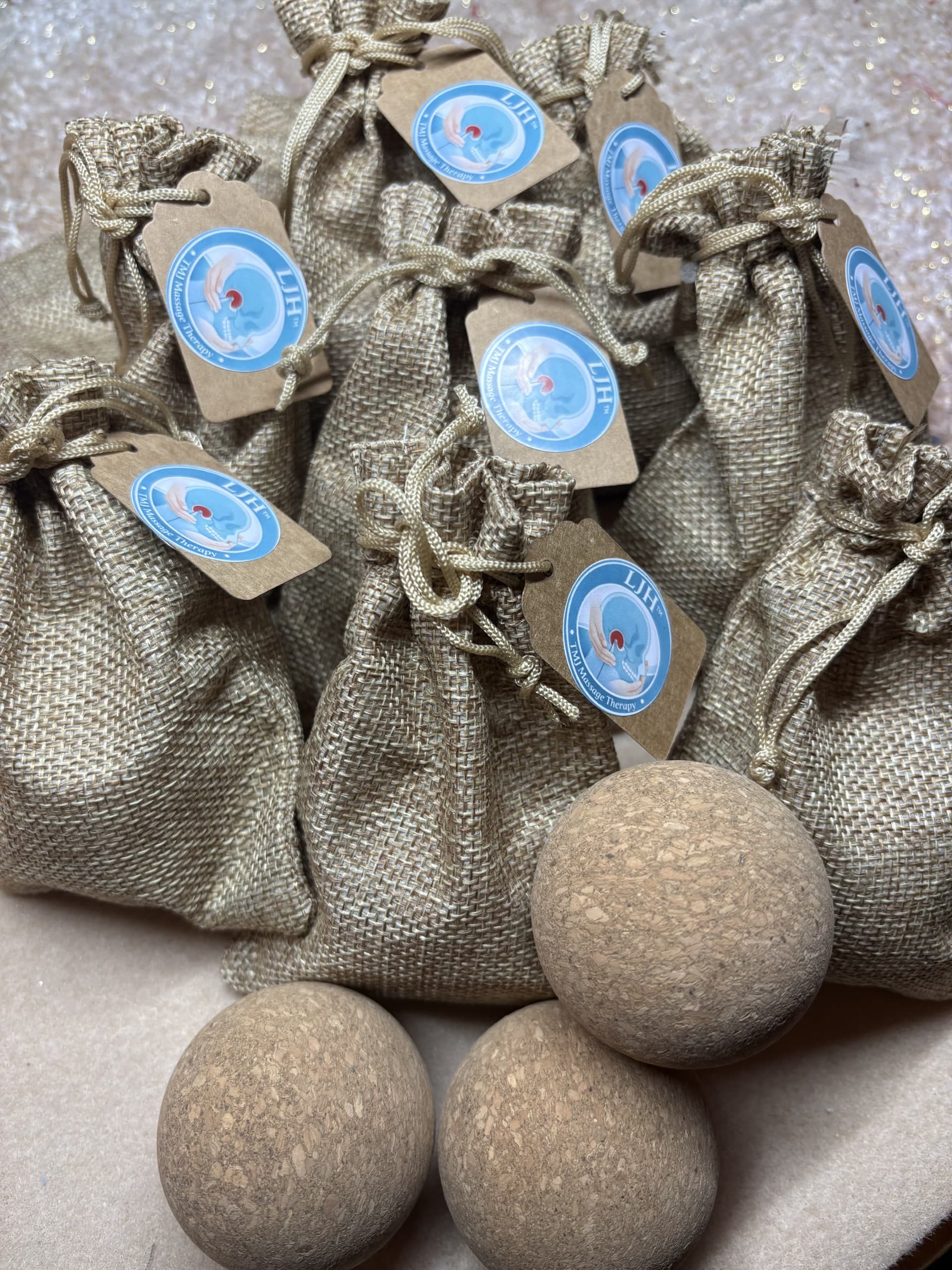 Burlap bags with LJH TMJ Massage Therapy tags and three round cork massage balls.
