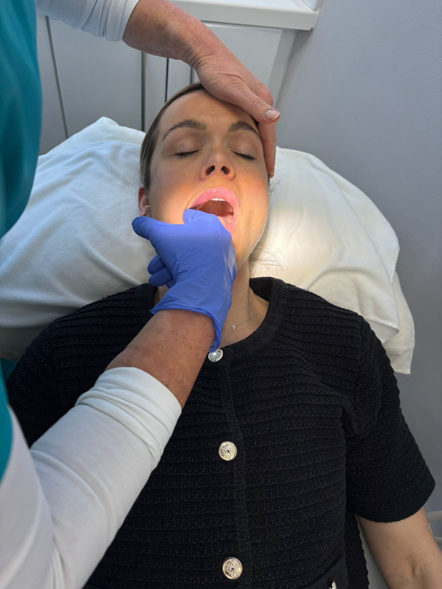 Practitioner performing an intraoral massage on a woman lying down with her eyes closed.